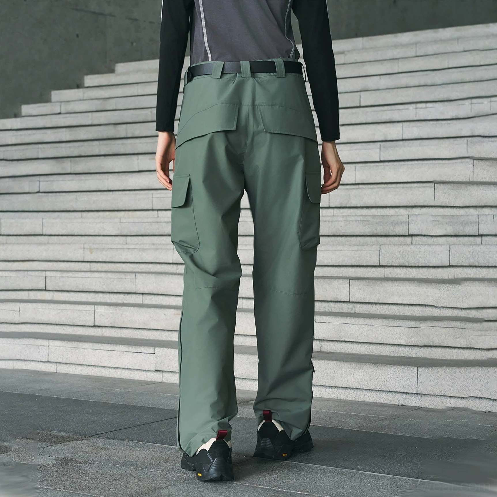 Sage green techwear cargo pants shown from the front with multiple utility pockets, belt styling, and a loose straight-leg streetwear cut