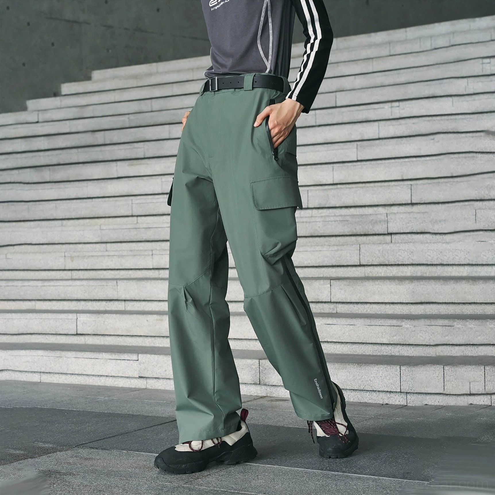 Sage green waterproof streetwear cargo pants shown in a full side view with thigh pockets, technical zipper details, and hiking boot styling