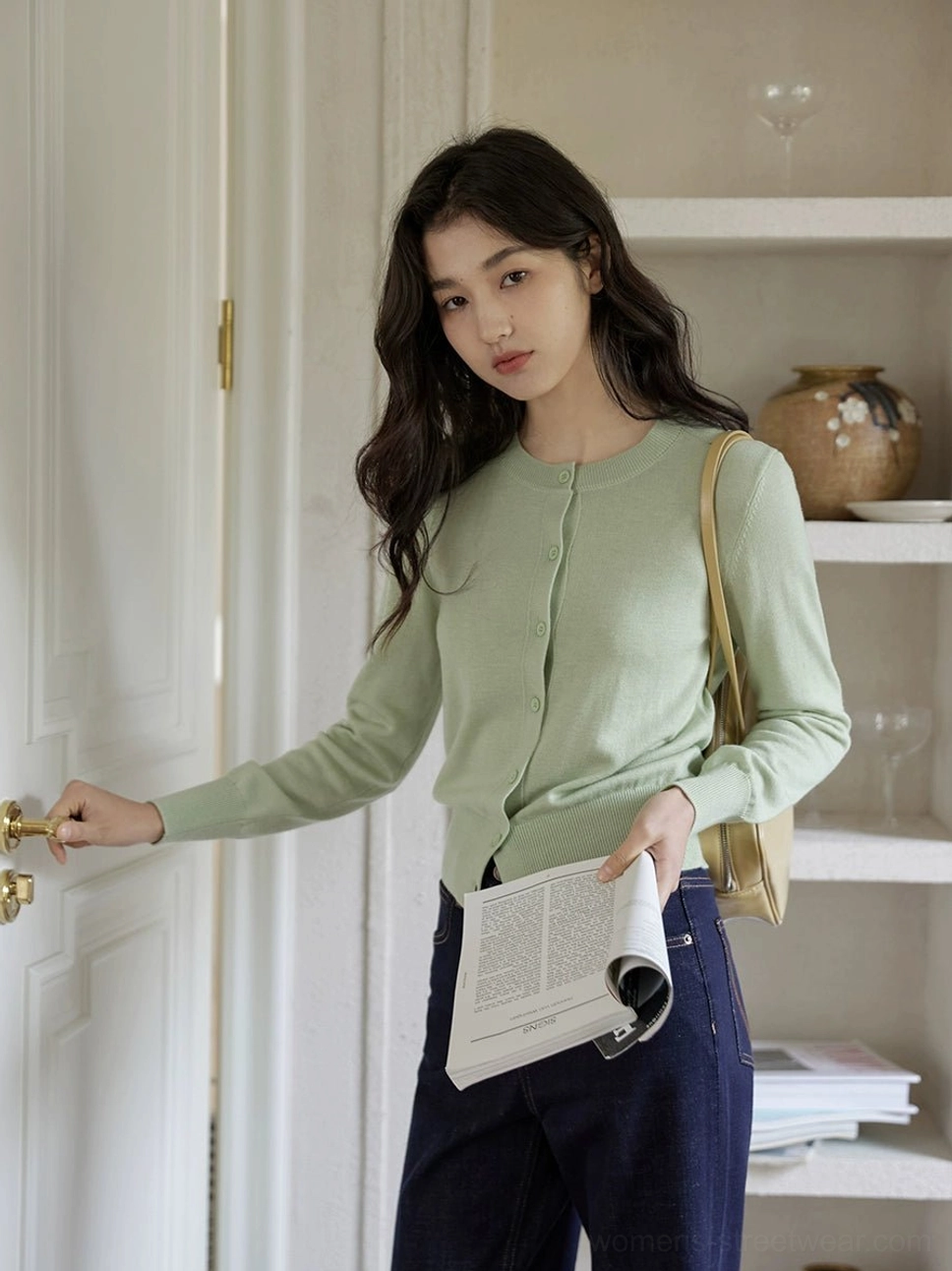Sage mint green women's fine-knit button-front cardigan styled with dark jeans and a tan shoulder bag in a casual hallway