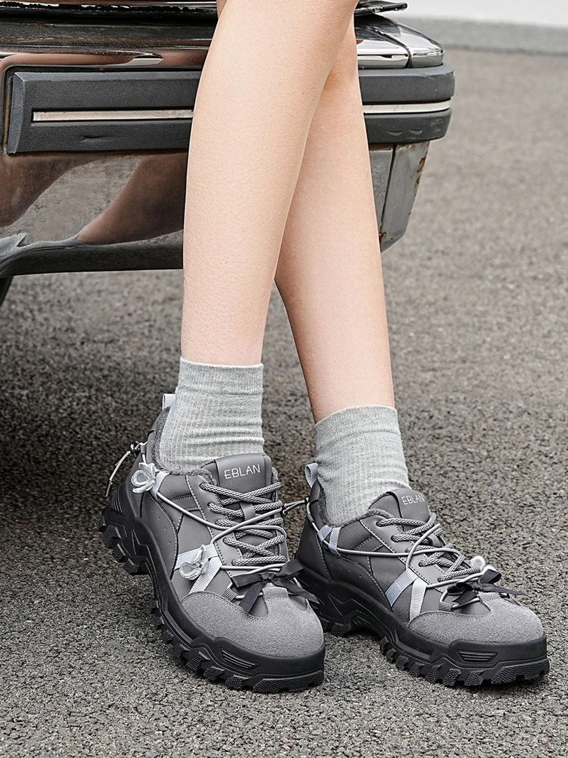 Dark grey plush lined chunky trail sneakers worn with grey crew socks in an outdoor roadside setting showing everyday gorpcore streetwear styling