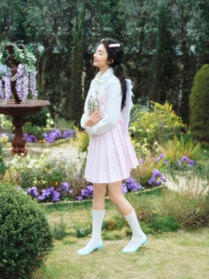 Model wearing light blue satin bow low block heel ballet pumps with a pastel preppy outfit in a flower garden