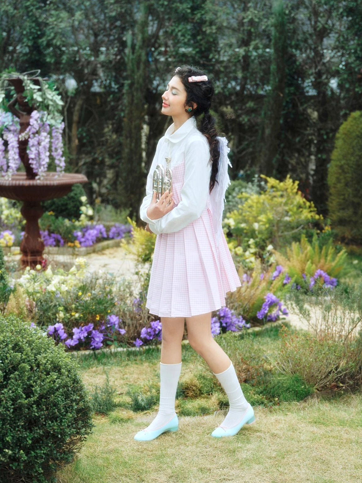 Model wearing light blue satin bow low block heel ballet pumps with a pastel preppy outfit in a flower garden