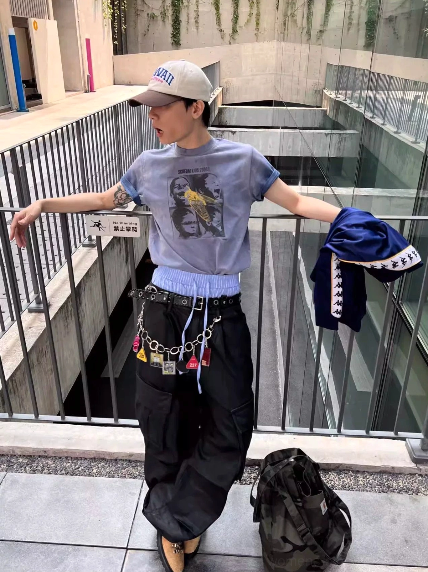 Male model in a baseball cap wearing a dusty blue Scream Kids printed graphic tee with layered streetwear and waist chain details