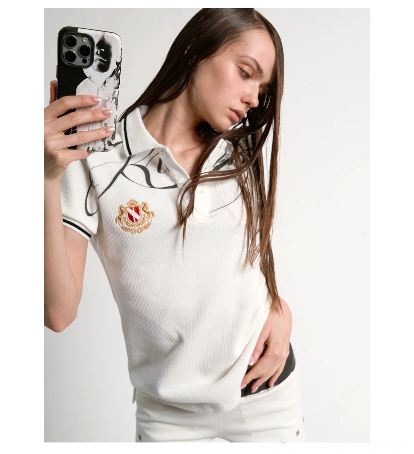 Female model close-up wearing white script crest polo with black trimmed collar and chest graphic
