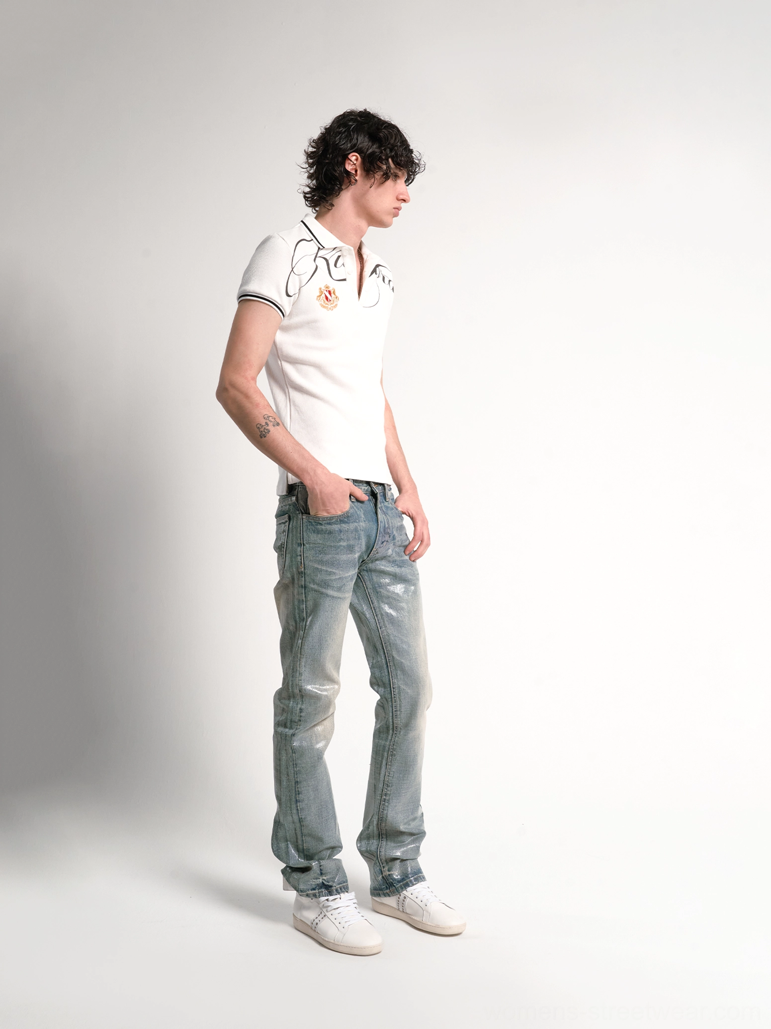 Side view of white script crest polo shirt styled with faded blue jeans and white sneakers