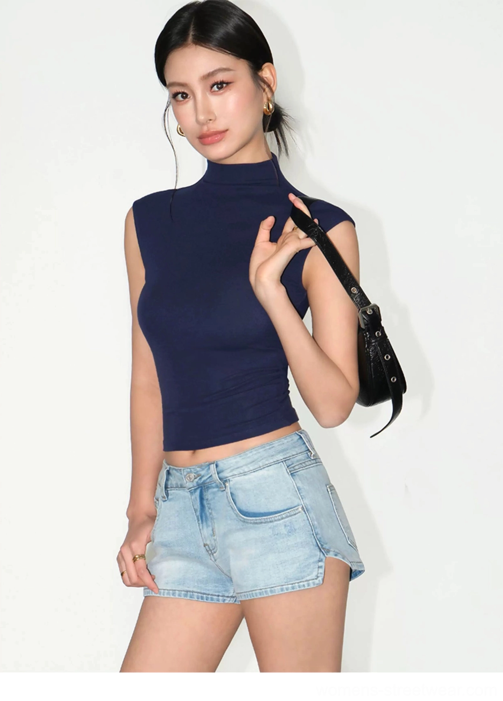 Royal blue fitted mock neck sleeveless cropped top side view with denim shorts and black shoulder bag