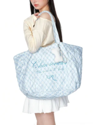 Sea salt blue oversized quilted plaid tote bag with rhinestone bow detail and fluffy bone charm shown from the rear on a streetwear model