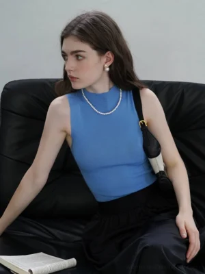 Blue sleeveless mock neck wool knit tank top styled with black maxi skirt in seated side view