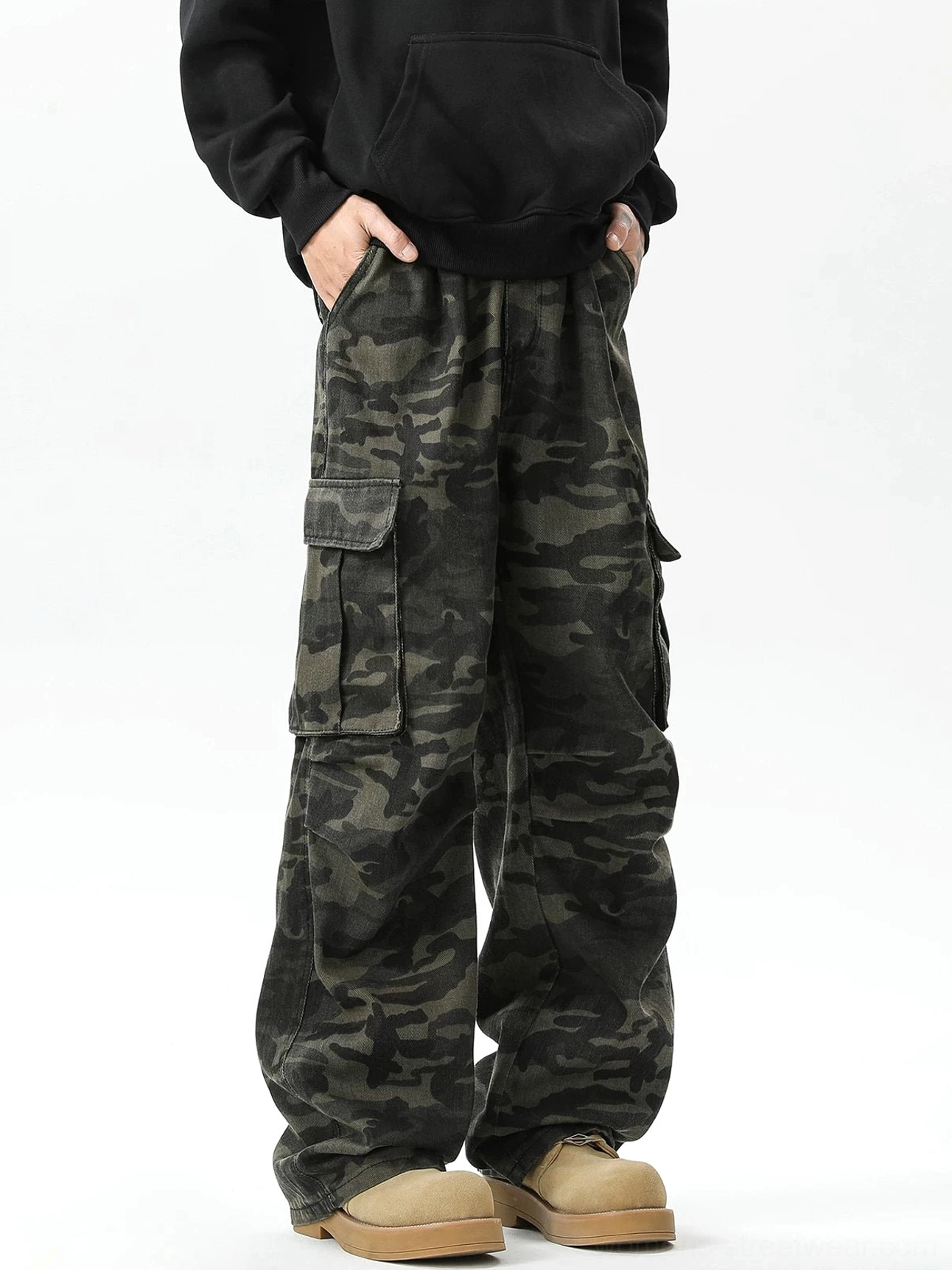 Front low-angle view of dark military green camouflage wide-leg cargo pants with oversized flap pockets styled with a black hoodie and chunky boots