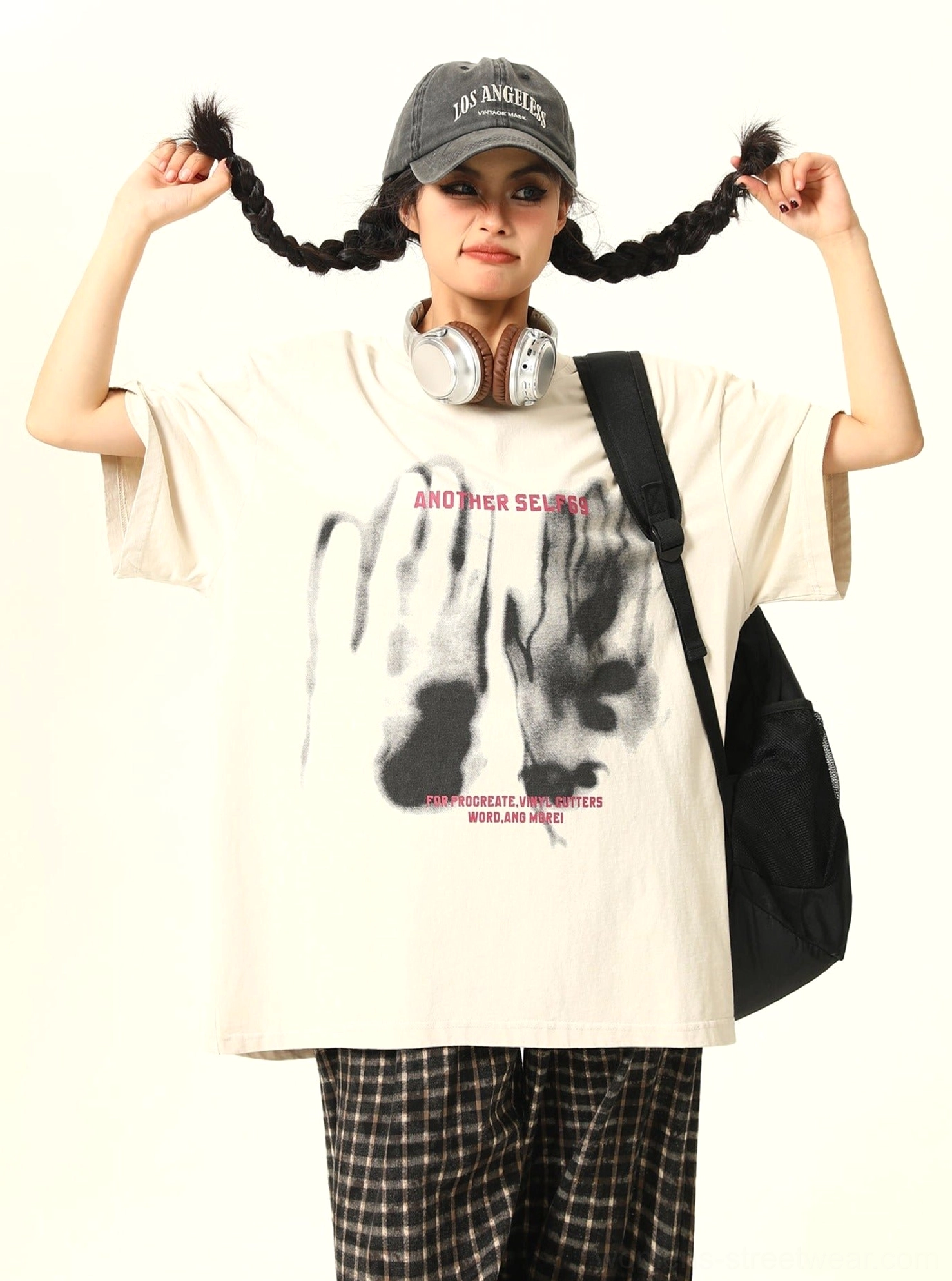 Apricot oversized shadow print selfie graphic T-shirt with black hand print and pink statement lettering styled with a baseball cap headphones plaid pants and backpack