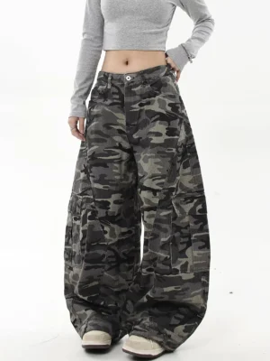 Left front three-quarter view of oversized dark woodland camouflage cargo jeans with wide legs, thigh pockets, and cropped grey streetwear top