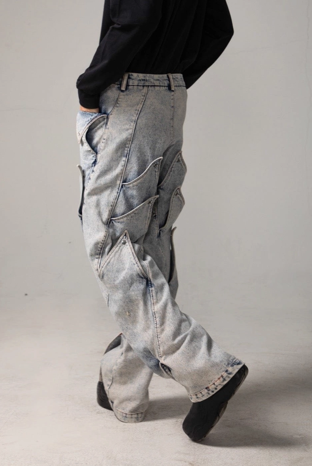 Left rear three quarter view of acid wash baggy jeans with shark fin side panels, belt loops, and loose streetwear fit