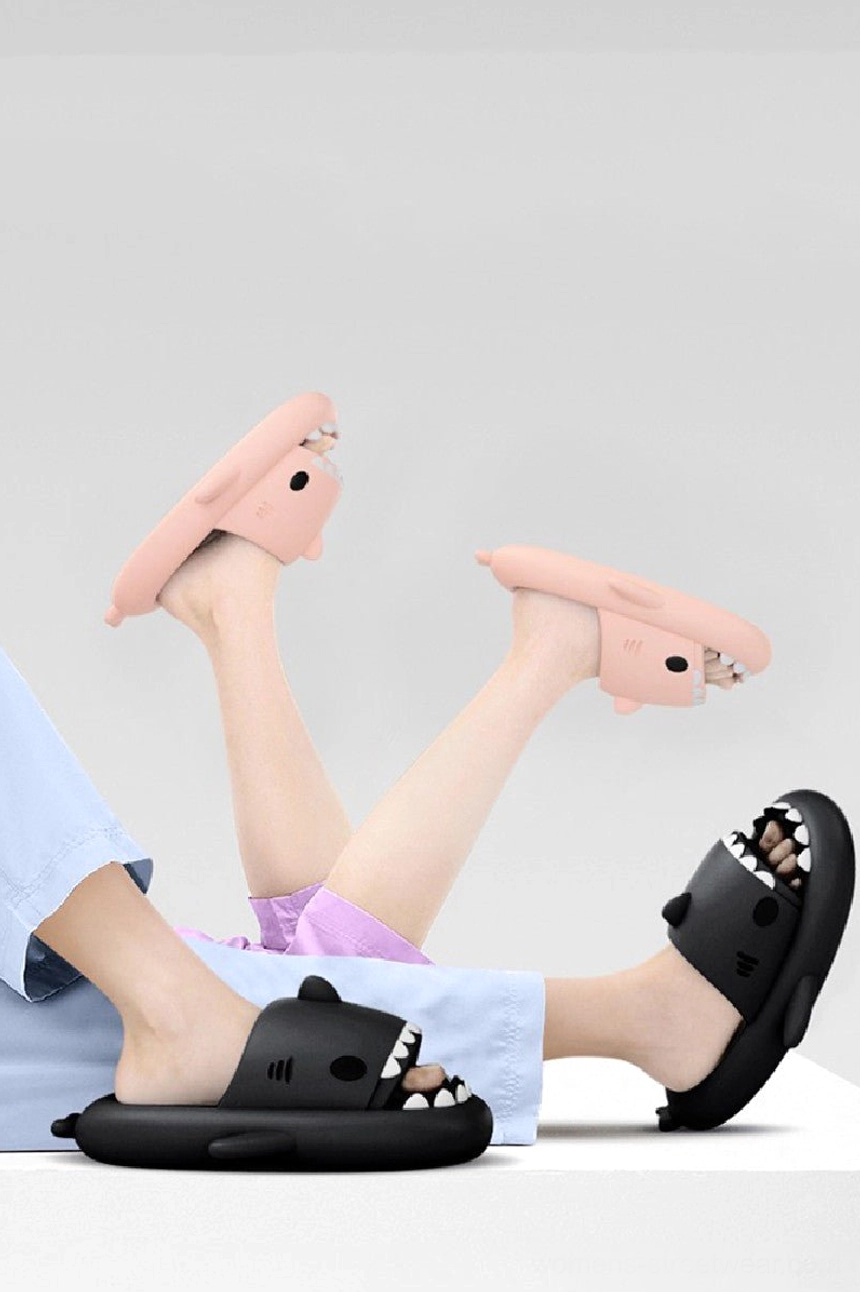 Shark slide slippers worn indoors with open-toe design, thick cushioned EVA sole, and playful pink and black color options