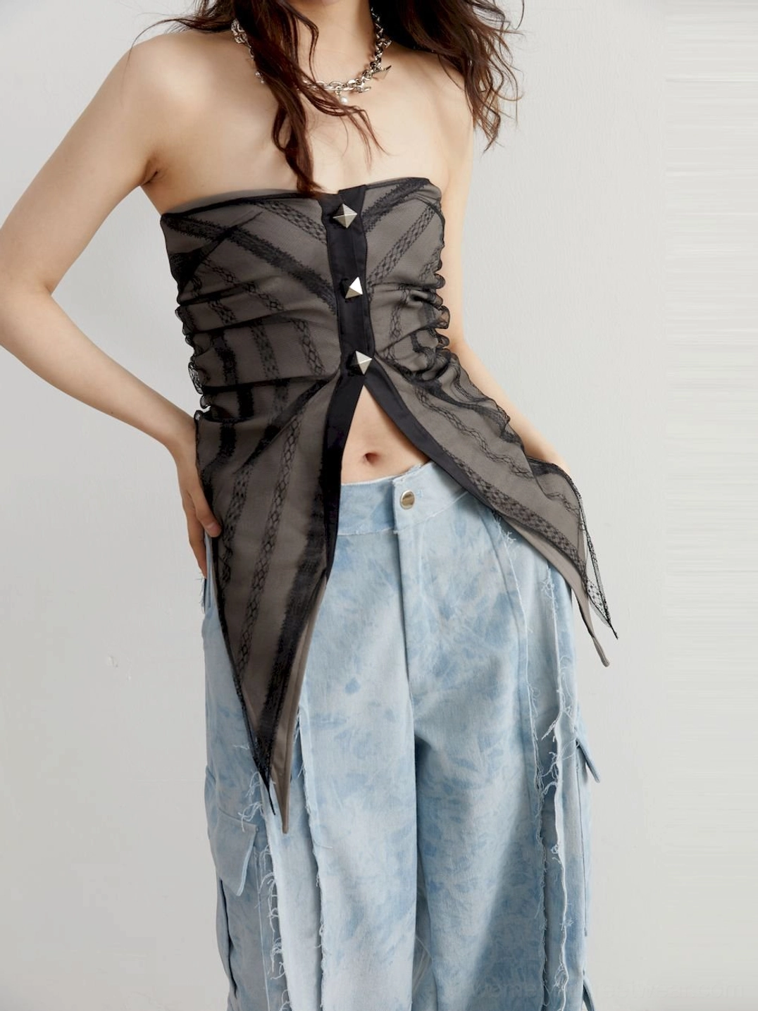 Front left view of a gray sheer asymmetric studded tube top styled with wide-leg cargo jeans and a silver chain necklace