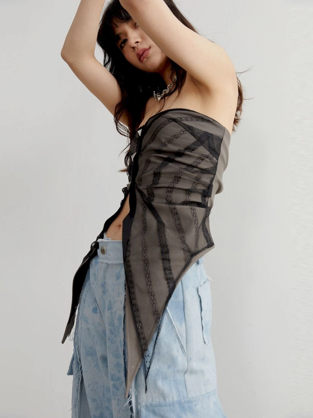Right angled styling view of a sheer checkered asymmetric tube top layered with wide-leg cargo denim