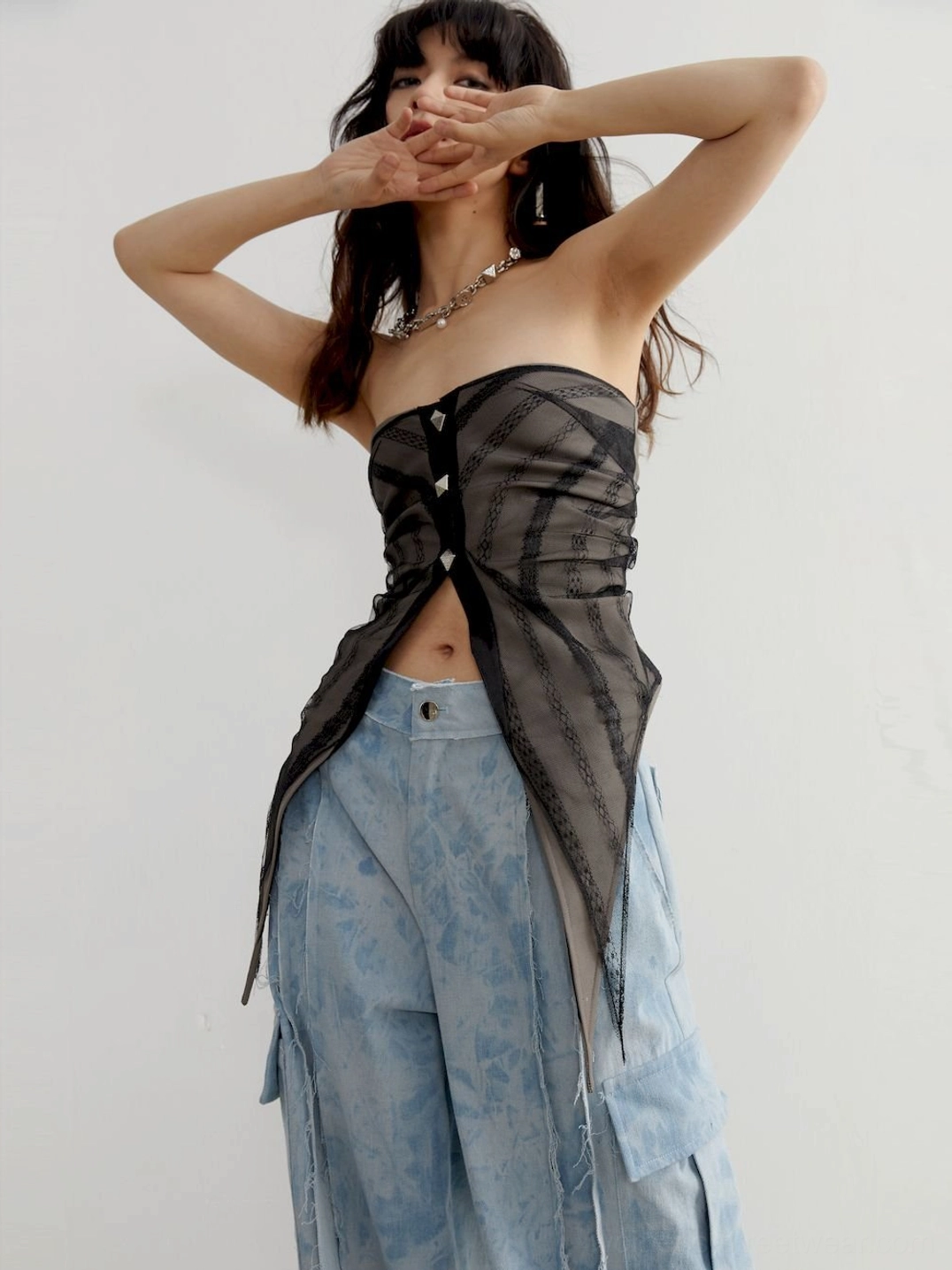 Right angled view of a sheer gray asymmetric tube top showing ruched shaping, exposed waist, and split pointed hem
