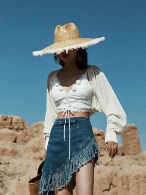 Beige apricot sheer knit batwing shrug cardigan layered over a lace-up crop top with fringe denim mini skirt