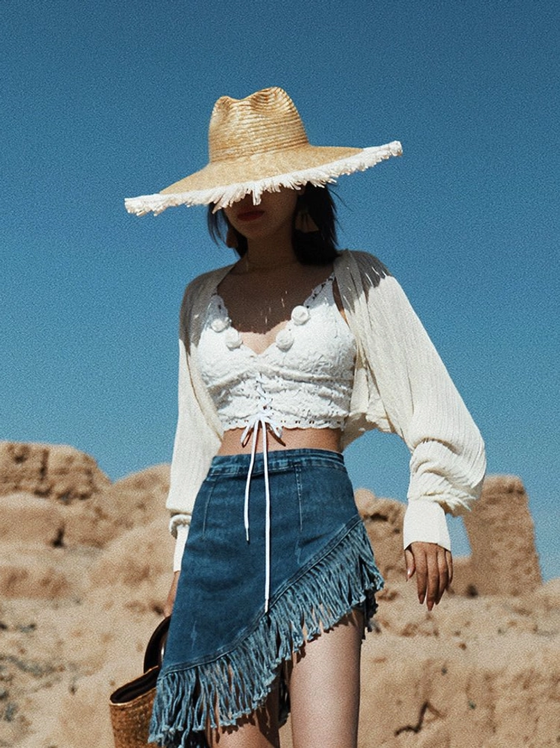 Beige apricot sheer knit batwing shrug cardigan layered over a lace-up crop top with fringe denim mini skirt