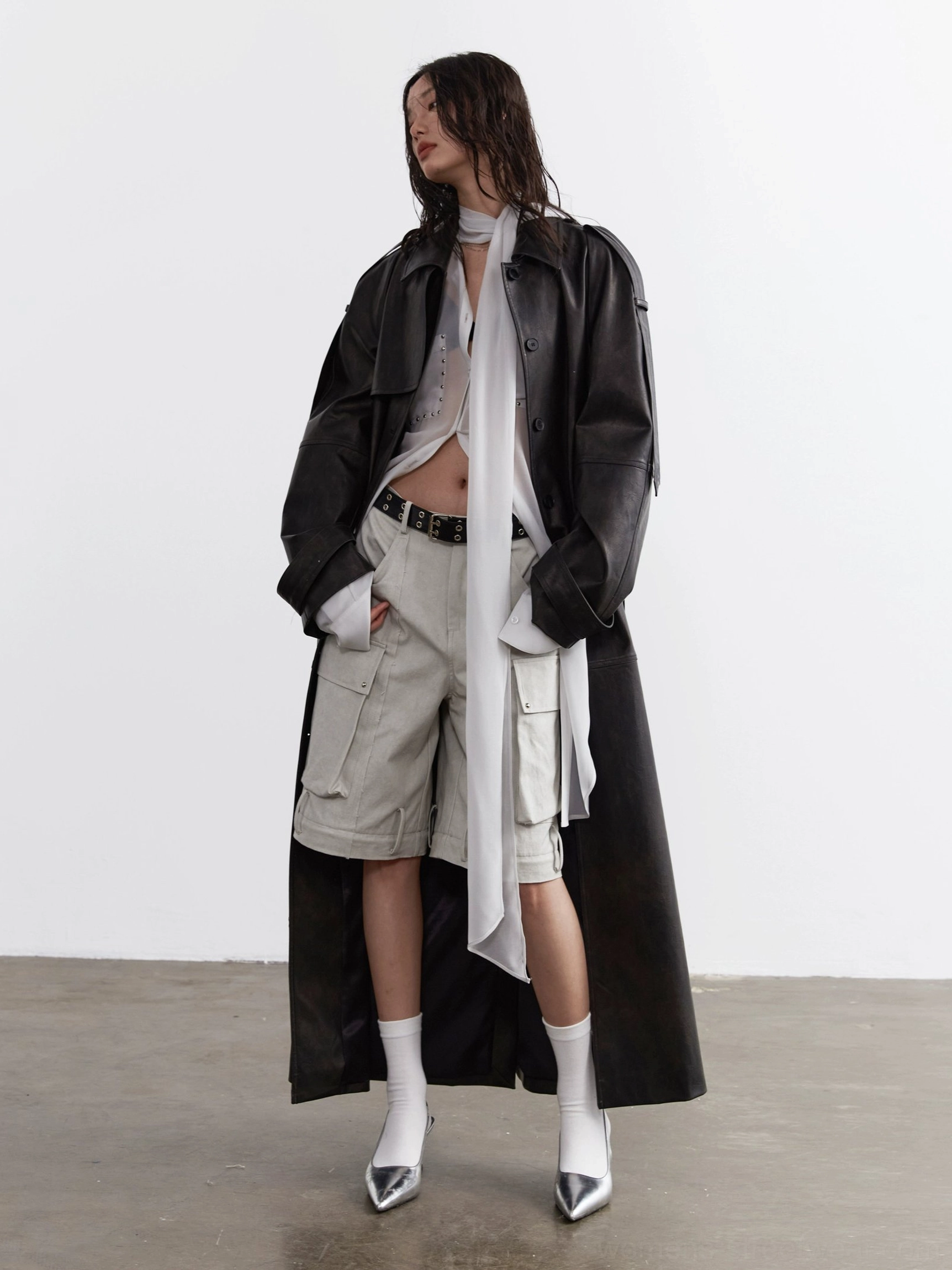 Sheer neck-tie blouse layered under a black faux leather trench coat with cargo shorts