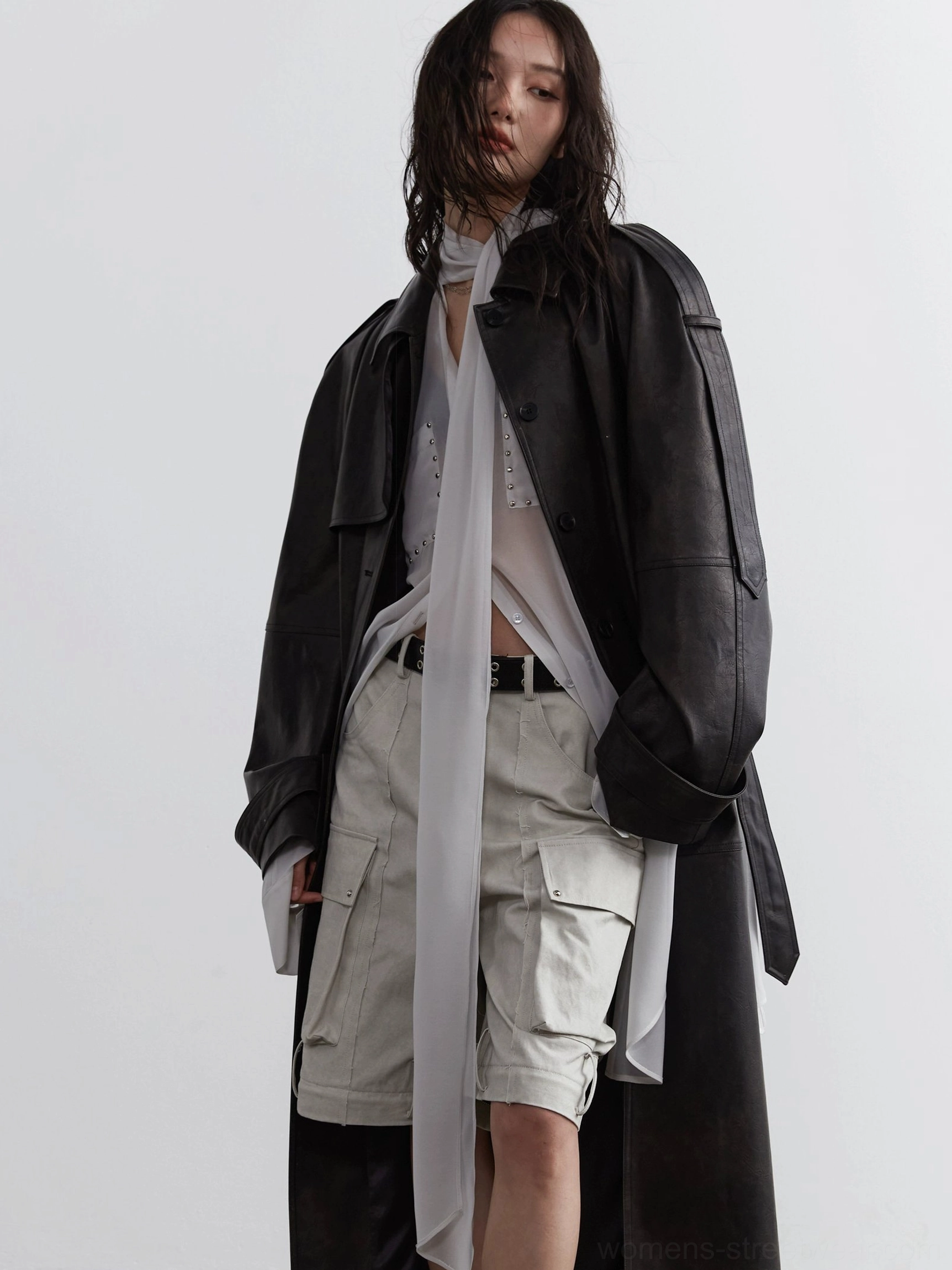 Side styling view of sheer blouse with attached scarf tie beneath a long black faux leather coat