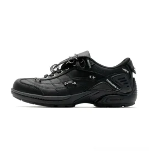 Black shield flap studded low-top streetwear sneaker shown in left side studio profile with layered synthetic upper and metal hardware details