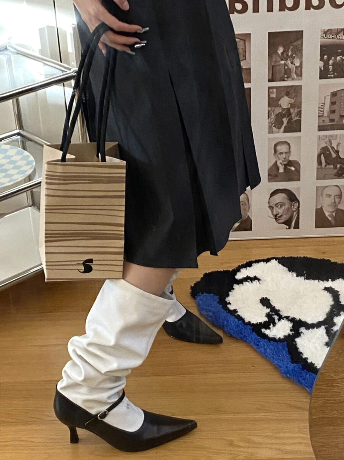 Side profile of a model wearing a black and white two-tone pointed-toe knee-high boot with relaxed white leg, black heel, and buckle ankle strap