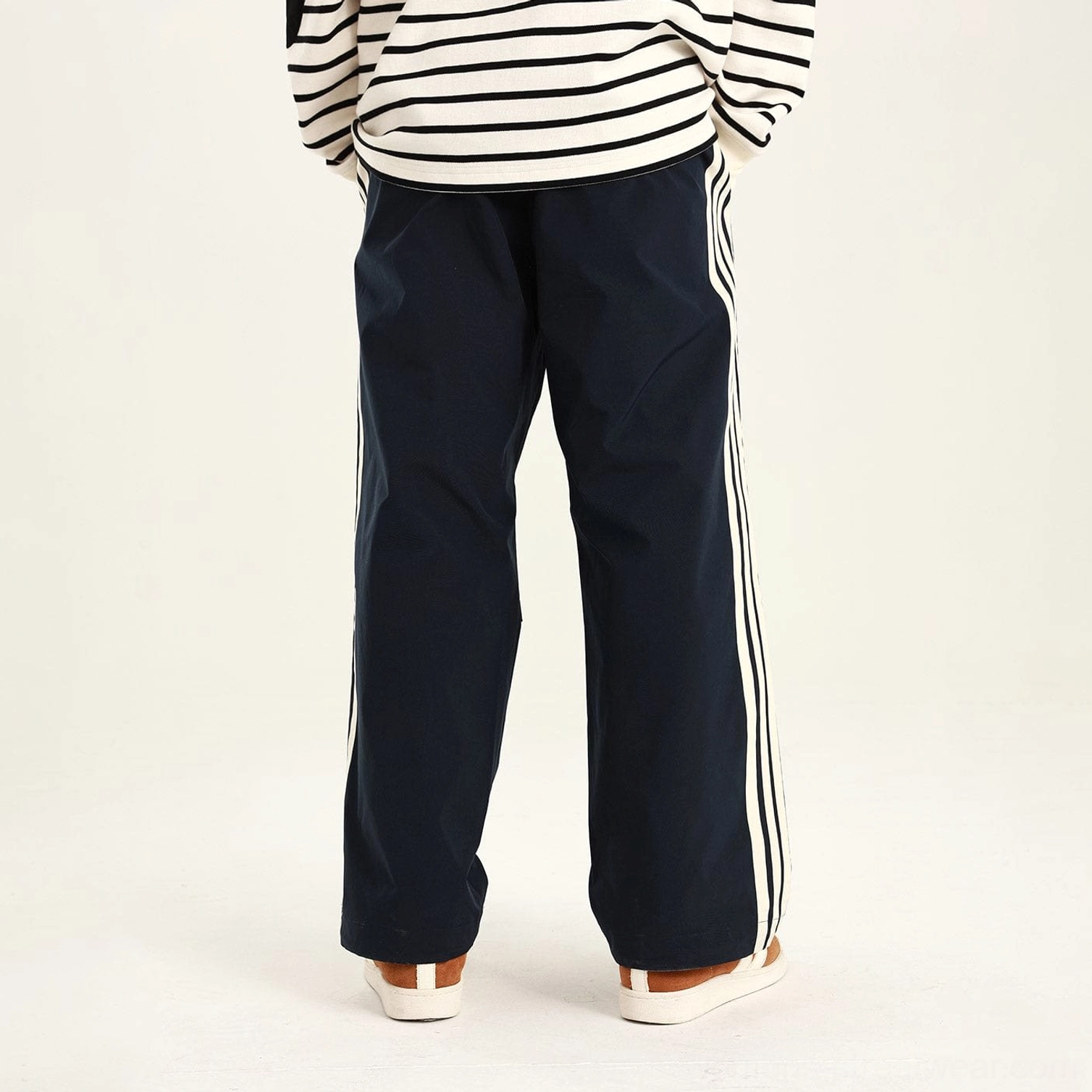 Blue side-stripe streetwear pants with white triple side stripes and articulated knees shown at an angle