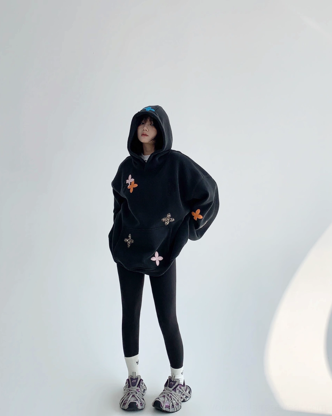 Side view of a black oversized floral hoodie with long dropped sleeves, mixed flower appliqués, and a loose cocoon-shaped streetwear fit