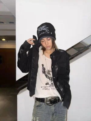 Female model wearing a cropped black faux leather trucker jacket with textured finish, graphic T-shirt, vintage denim jeans, and knit beanie in a casual streetwear outfit