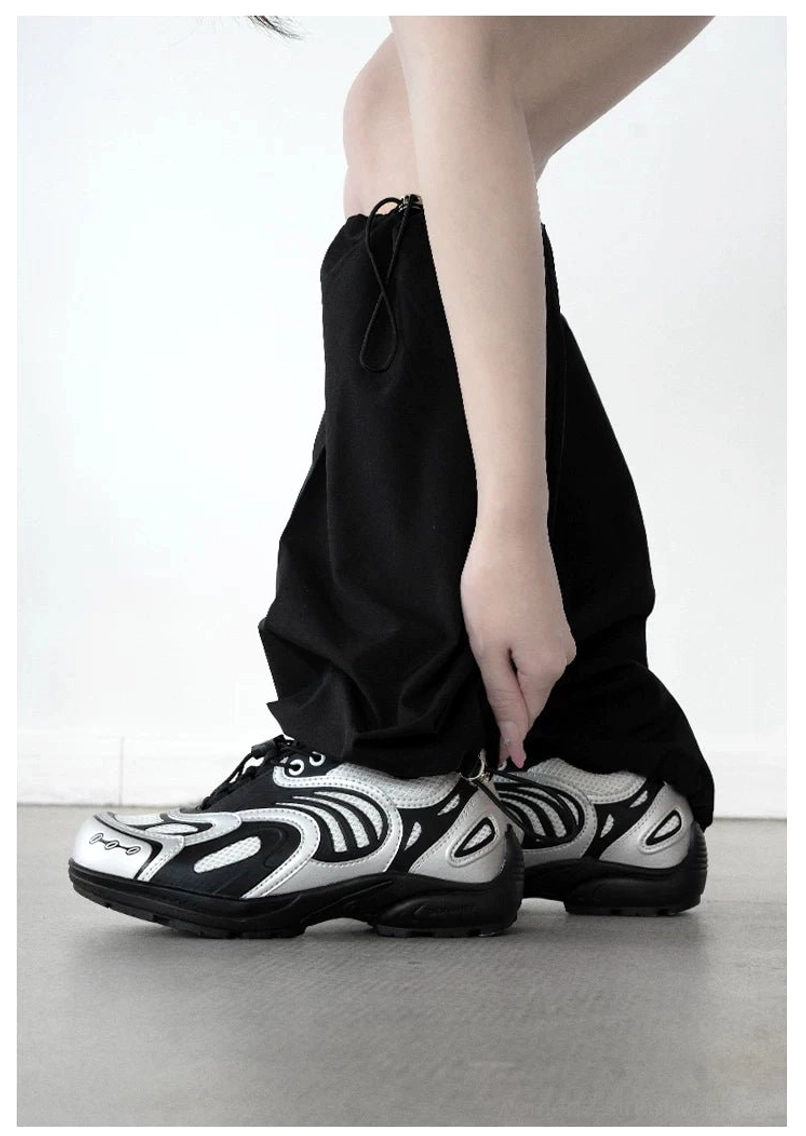 Rear side view of silver black techwear runner sneakers styled with black wide leg drawstring trousers in studio