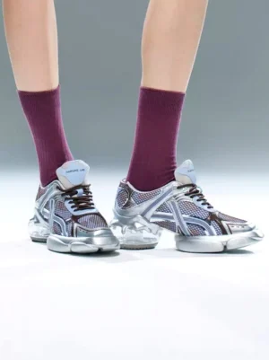 Silver-blue chunky running sneaker shown from a low front angle with burgundy socks, dark laces, layered mesh upper, and translucent thick outsole