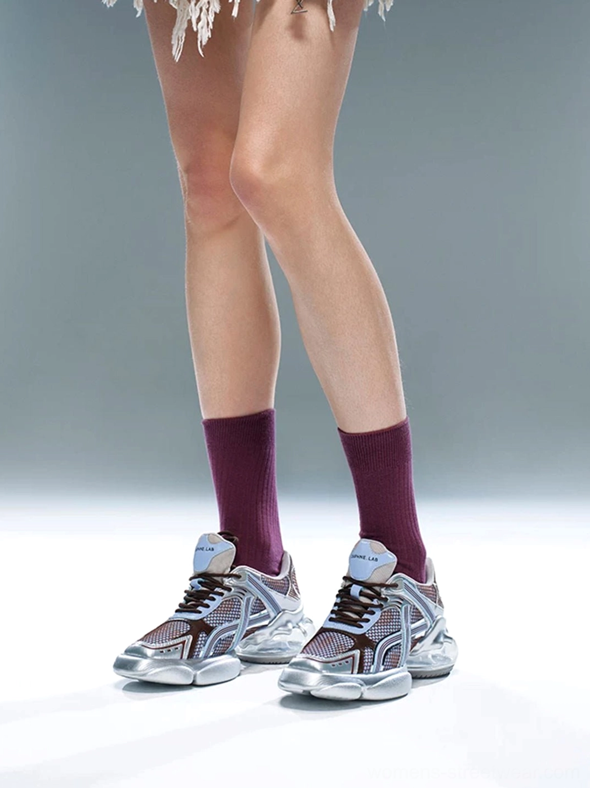 Pair of silver-blue mesh runner sneakers worn with burgundy socks and a fringed mini skirt, featuring a sculpted chunky outsole and retro Y2K styling