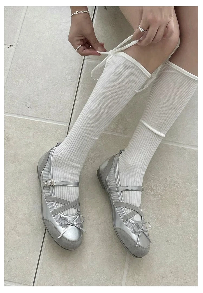 Top view of metallic silver bow ballet flats with adjustable crossover buckle straps styled with white ribbed socks