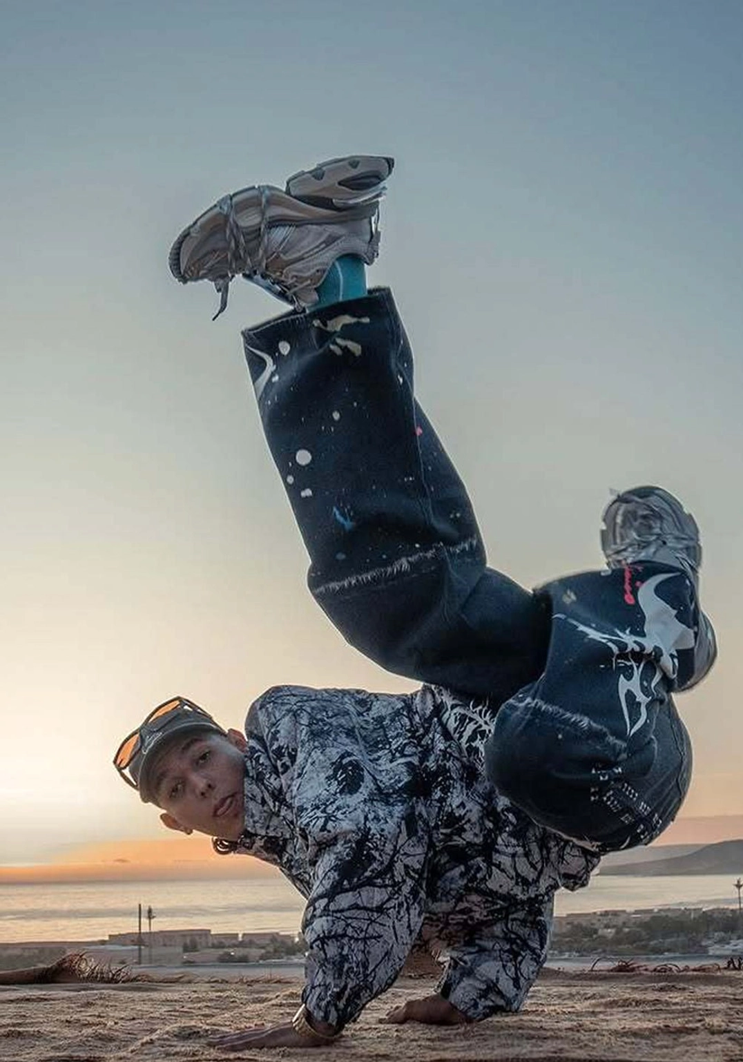 Silver chunky dance sneakers worn during an outdoor street dance performance with a seaside sunset background