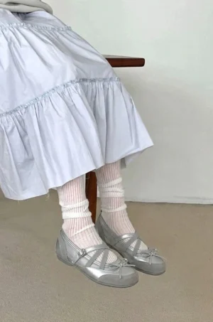 Woman wearing silver cross strap Mary Jane ballet flats with white ribbed socks and a light blue ruffled skirt