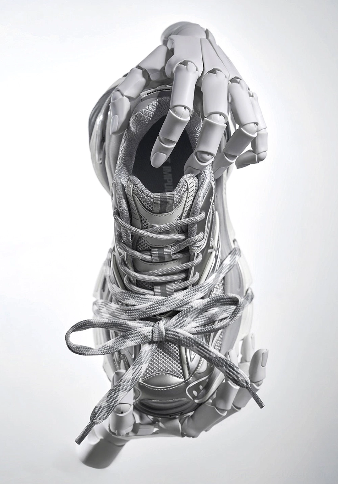 Silver futuristic chunky streetwear sneakers held by metallic robotic hands showing camo patterned laces and thick rubber outsole