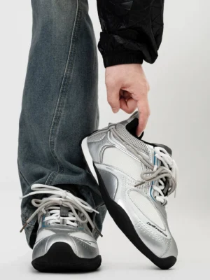 Silver and light gray retro runner sneakers with breathable mesh panels, metallic toe cap, layered upper, and washed blue straight-leg jeans