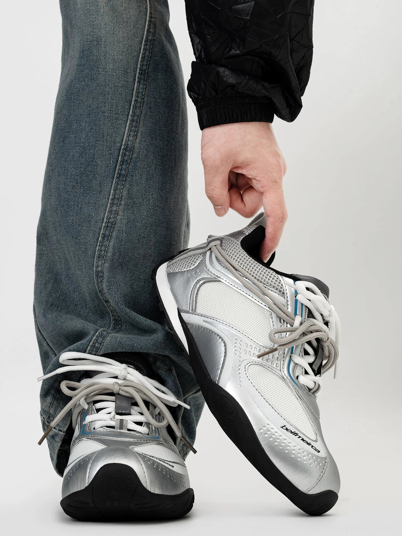 Silver and light gray retro runner sneakers with breathable mesh panels, metallic toe cap, layered upper, and washed blue straight-leg jeans