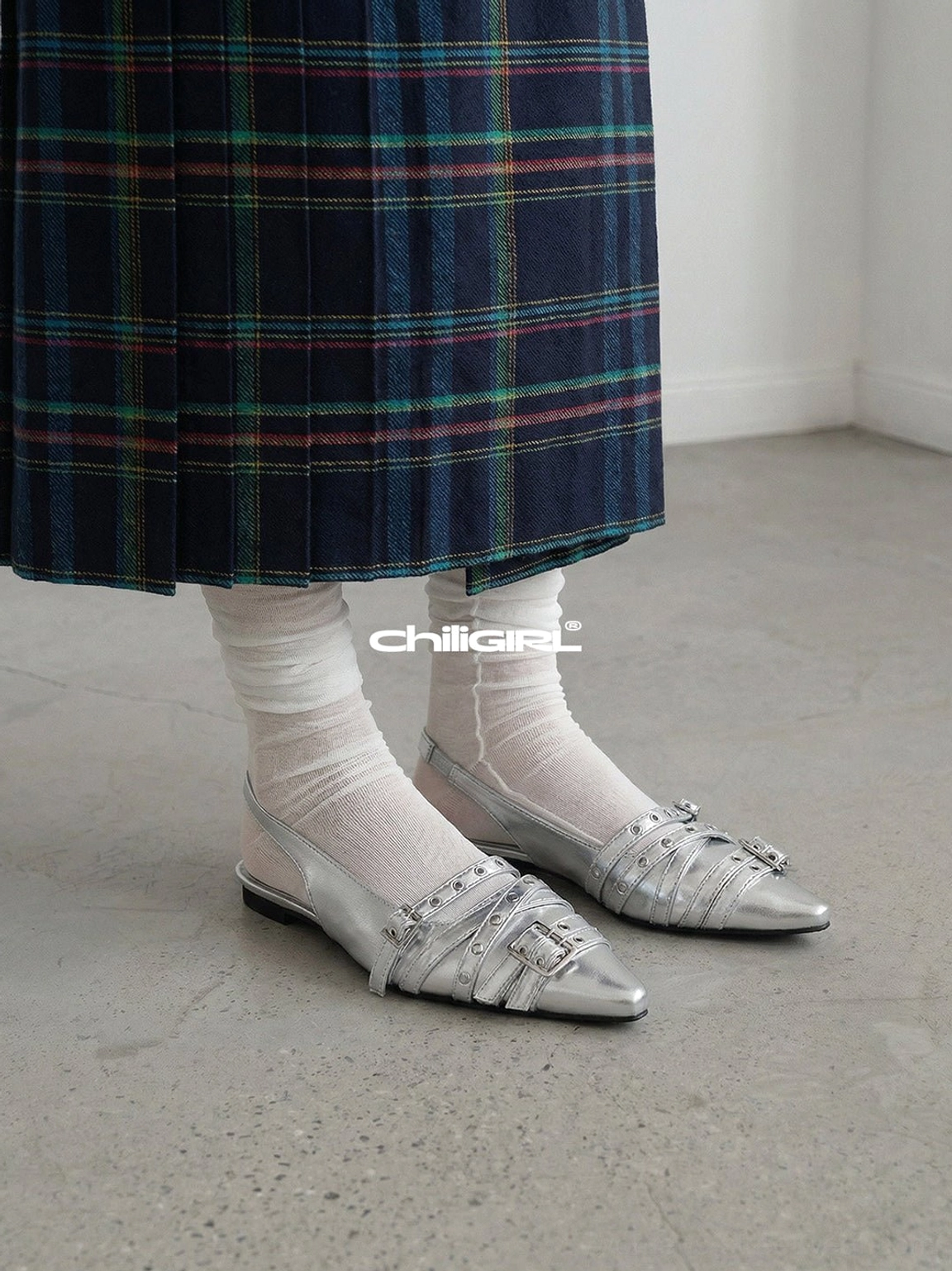 Silver metallic pointed-toe flats with double buckle straps styled with sheer socks and a dark green plaid pleated skirt