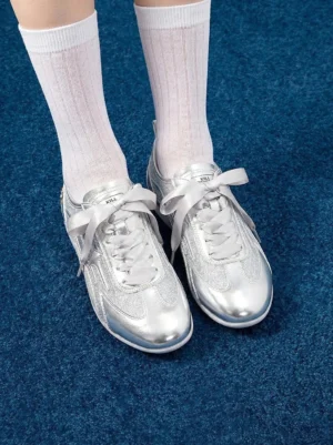 Top-down view of silver metallic streetwear trainers with bow-shaped ribbon laces, glittery panels, and white ribbed crew socks