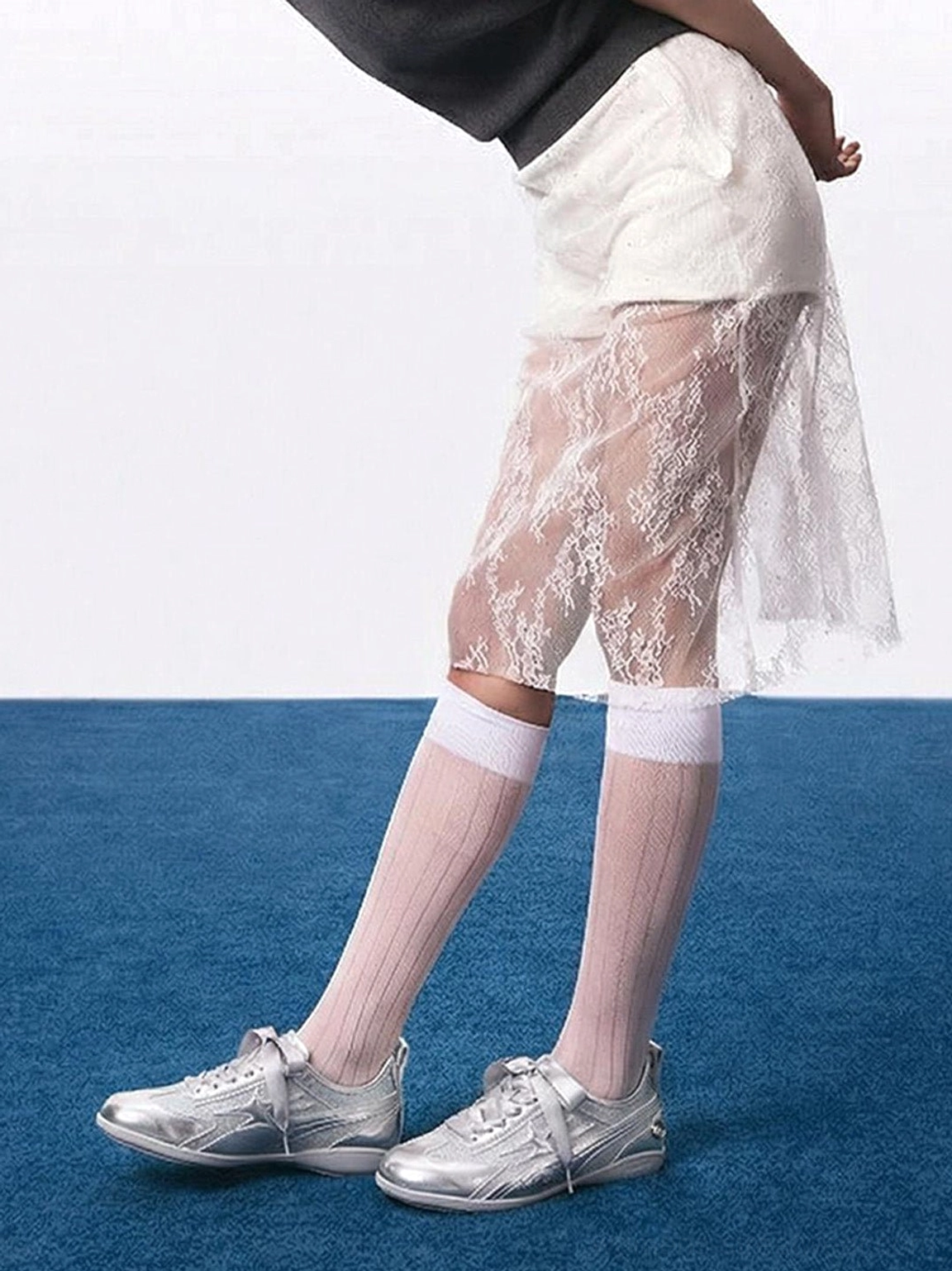 Full lower-body view of metallic silver women's trainers paired with pink ribbed knee socks and a sheer lace skirt