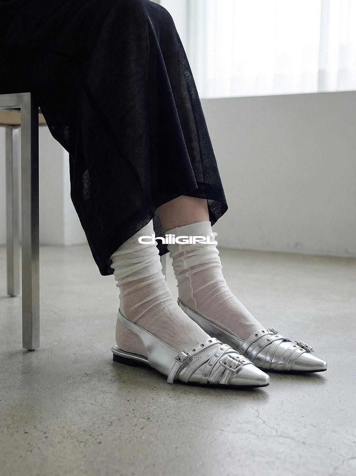 Side view of silver pointed-toe slingback flats worn with sheer white socks and loose black cropped trousers