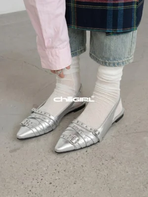 Model wearing silver pointed-toe slingback flats with double buckle straps, sheer white socks, a pink shirt, and denim