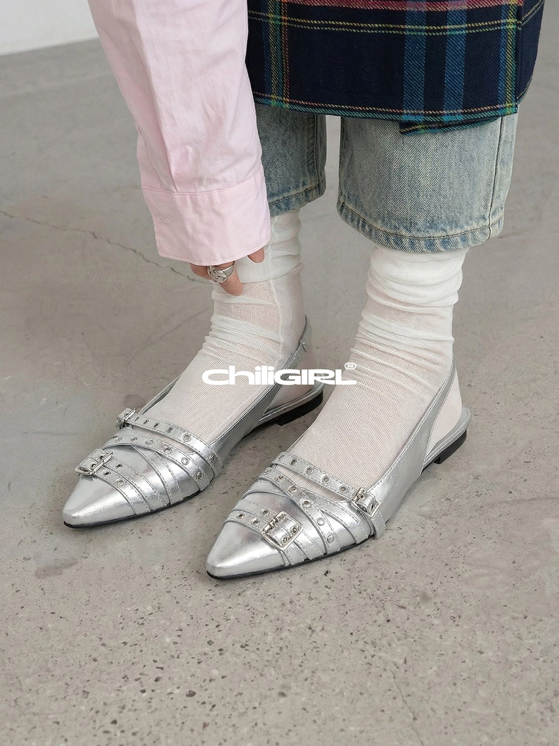 Model wearing silver pointed-toe slingback flats with double buckle straps, sheer white socks, a pink shirt, and denim