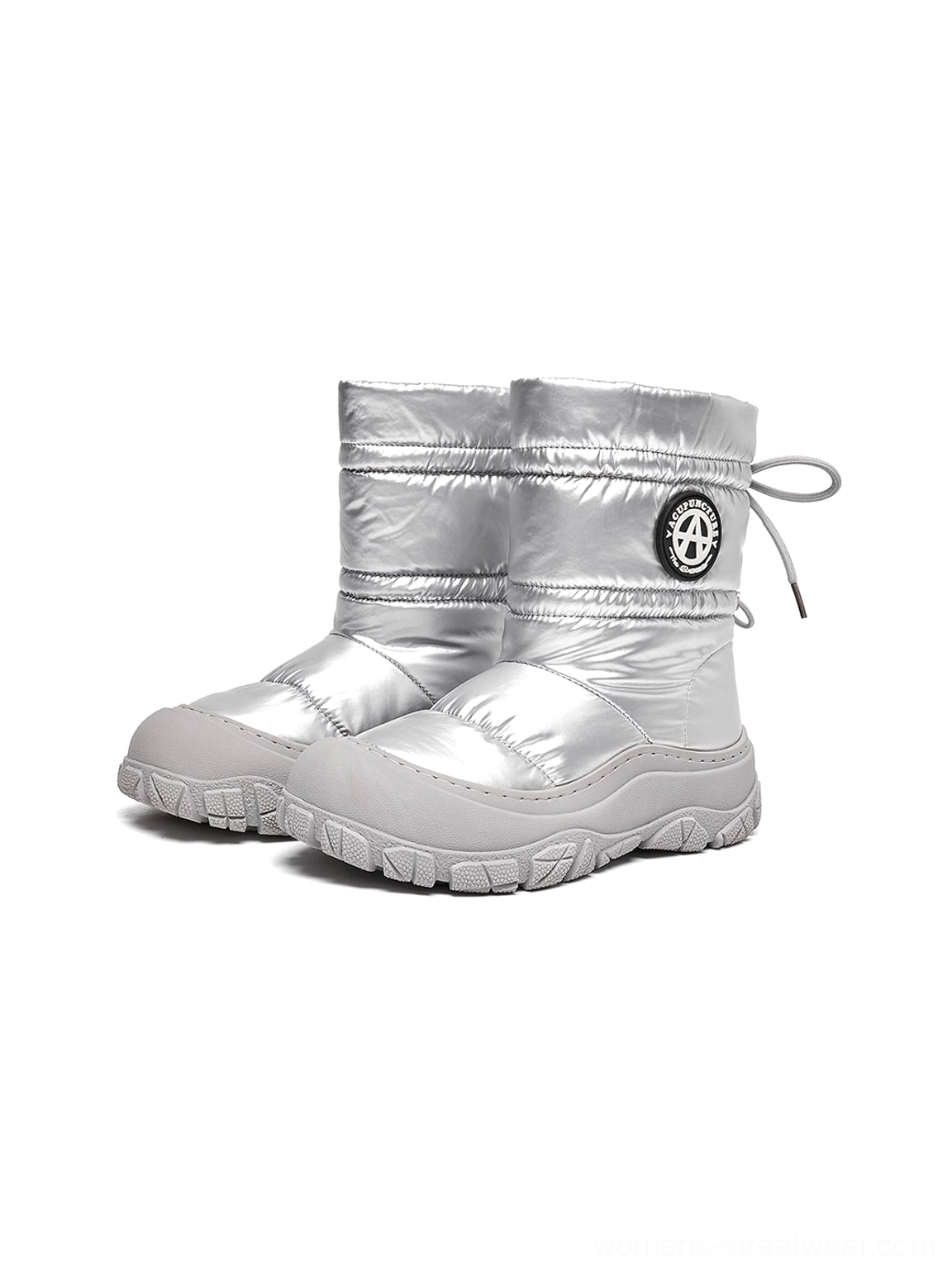 Pair of silver puffer snow boots in a three-quarter studio view with padded shafts, rear drawstring toggles, and circular collar badges