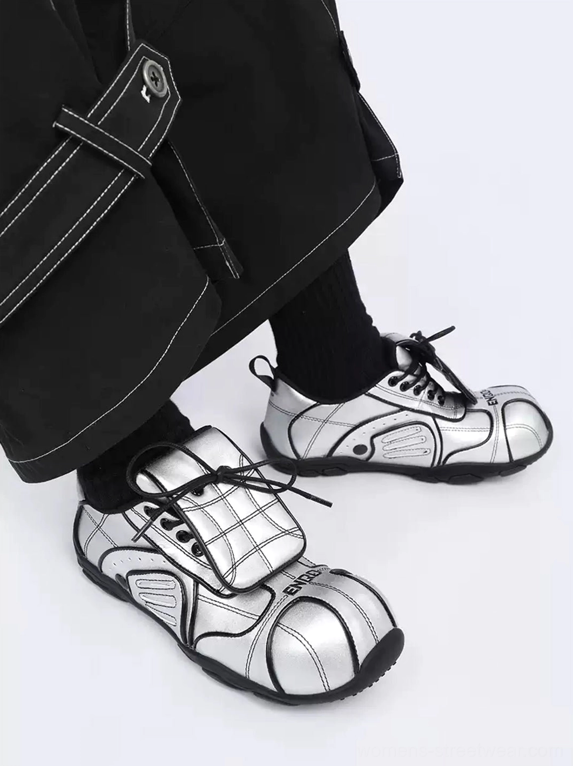Right-side styling view of silver quilted low-top streetwear sneakers with layered foldover tongues, black laces, and cargo trousers