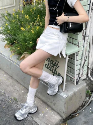 Model wearing silver rhinestone chunky dad sneakers with a black crop top and white mini skirt in a casual streetwear setting