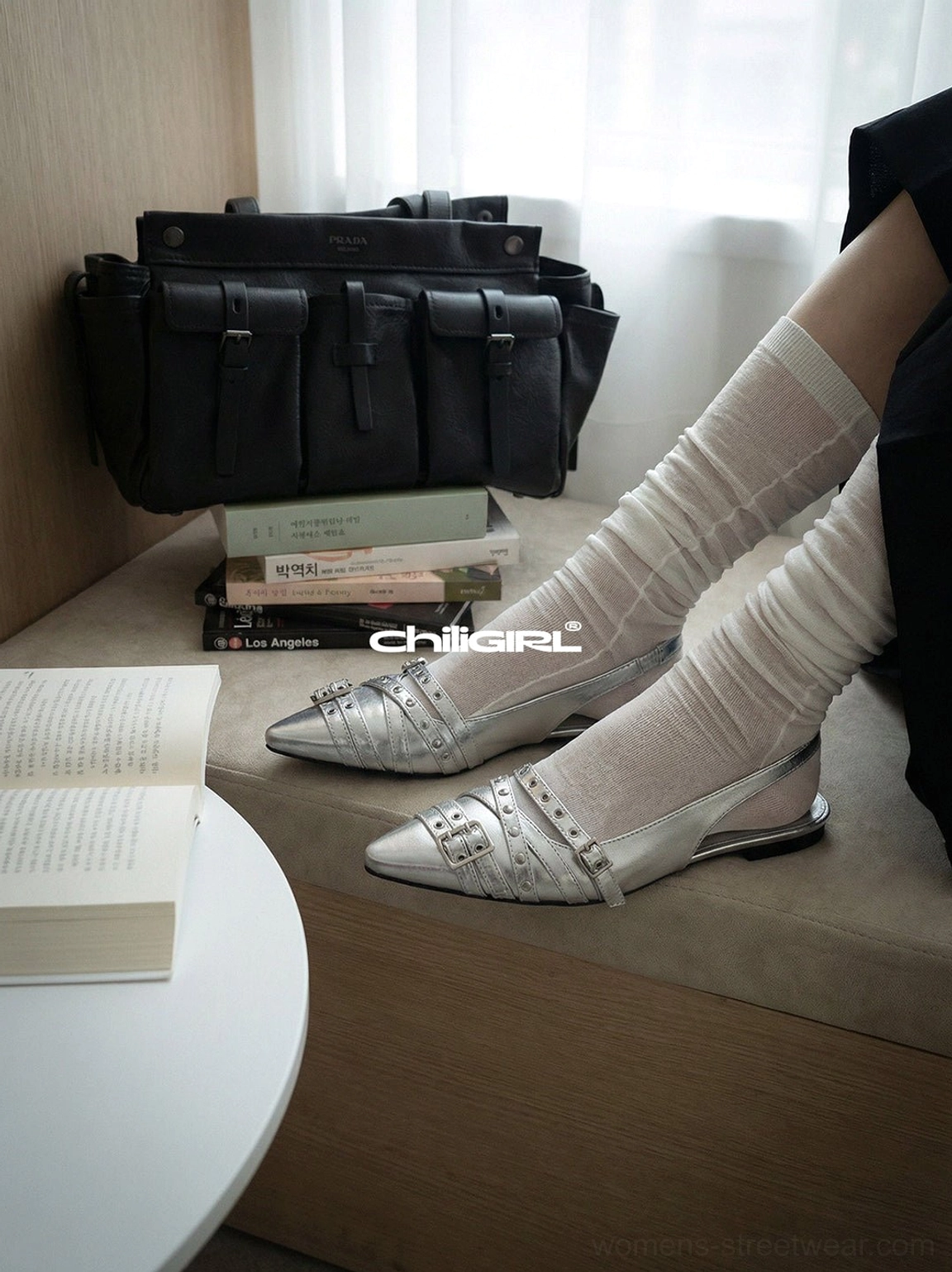 Silver slingback flats with pointed toe and adjustable buckle details displayed beside a black multi-pocket handbag and books