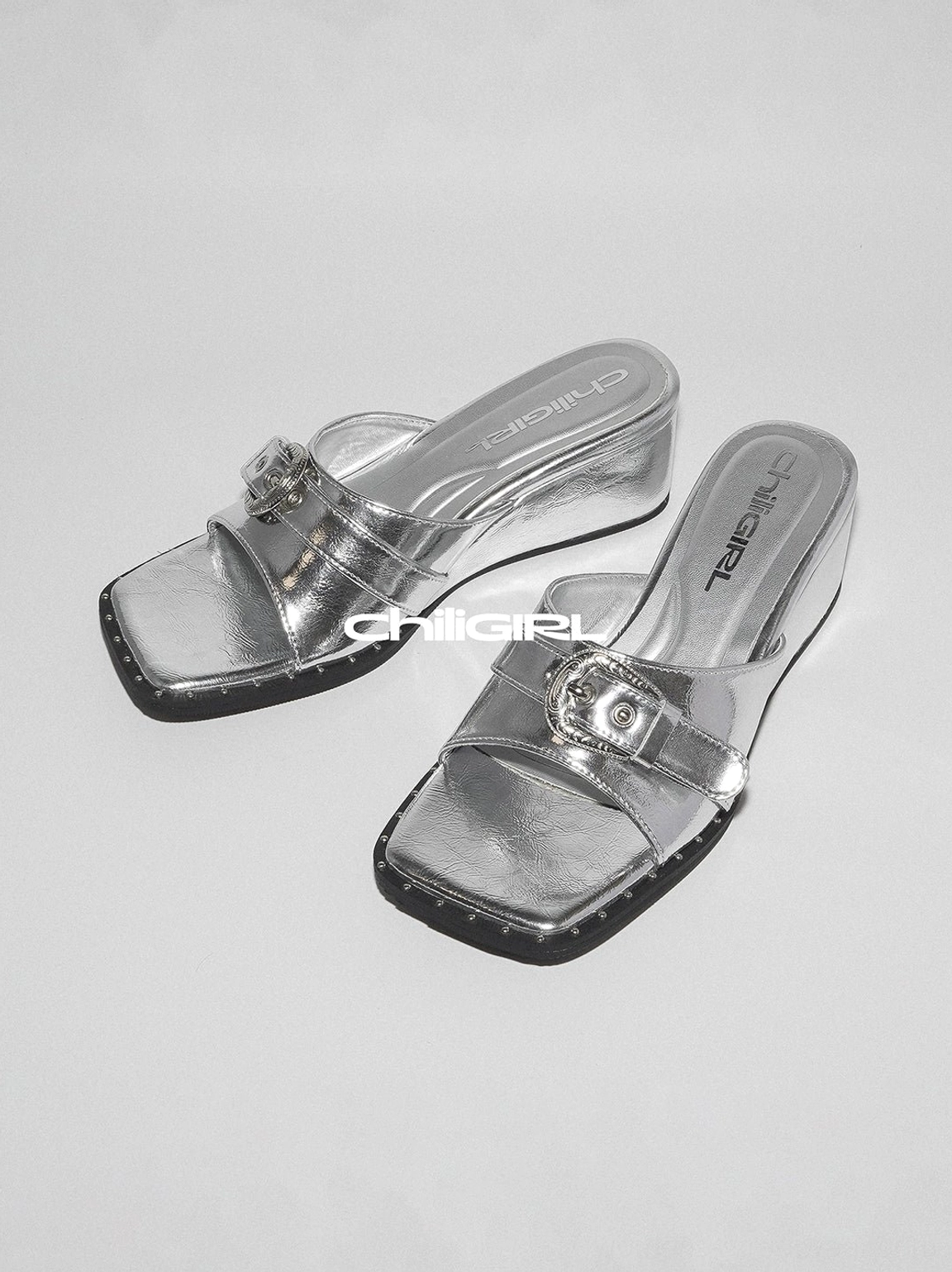 Silver square-toe low-wedge slide sandals with transparent strap polished buckle and studded sole