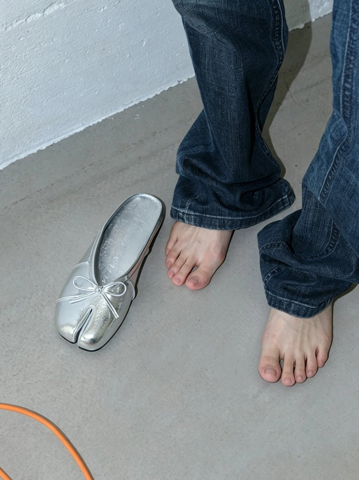 Model styling metallic silver tabi toe bow mules with baggy blue jeans for a modern Y2K streetwear look